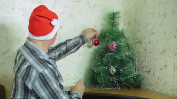Egy ember, egy Mikulás kalap díszíti a karácsonyfát, ünnepi léggömb. — Stock videók