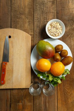 Beyaz tabak portakal, mango, kivi yalan ahşap bir masaya. dikey resim. üstten görünüm