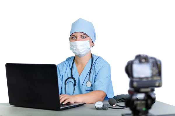 Женщина-врач в маске печатает на компьютере на белом фоне . — стоковое фото