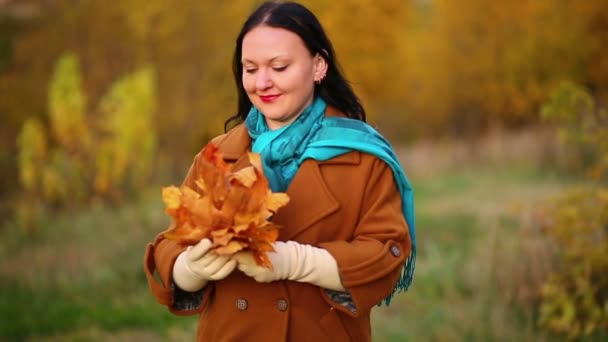 A young woman in the fall in the park admires a bouquet of maple leaves. Slow motion. — Stock Video