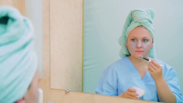 An actress in a dressing room at a table in front of a mirror puts a mask on her face with a brush. — Stock Video