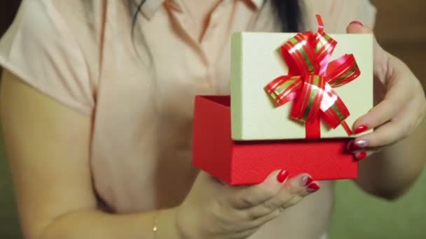 Een jonge vrouw opent een doos met een kerstcadeau en verheugt zich. — Stockvideo