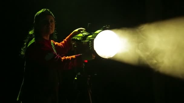 Una mujer iluminadora trabaja con un proyector de perfil y dirige un haz de luz . — Vídeos de Stock