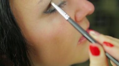 Genç bir esmer kadın göz gölgeler bir fırça ile uygulanır. Profil