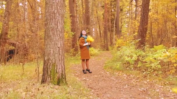 Молодая женщина в пальто и очках в осеннем парке с листьями в руках. Медленное движение . — стоковое видео