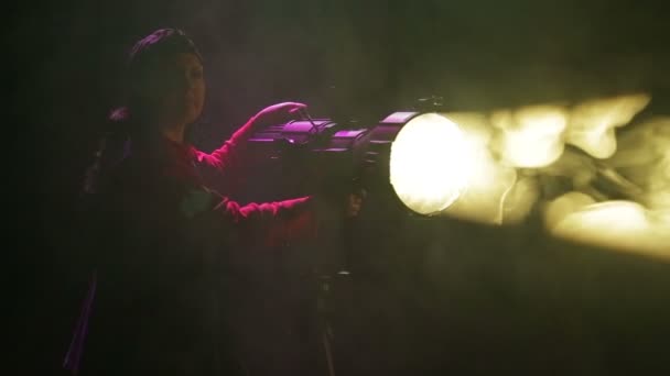 Una mujer iluminadora dirige un haz de luz desde un reflector de perfil — Vídeos de Stock