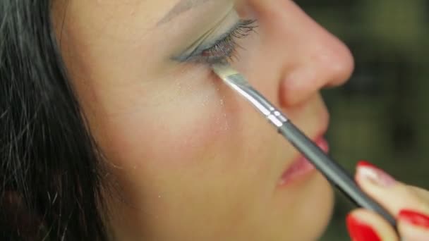 Een jonge vrouw nangosit eye shadows met een borstel. Profiel. — Stockvideo