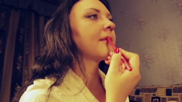 A young woman in a white robe paints the lips contour with a red pencil. — Stock Video