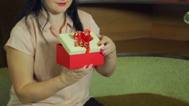 Μια νεαρή γυναίκα με καπέλο Αϊ-Βασίλη ανοίγει το κουτί με ένα δώρο Χριστουγέννων και χαίρεται. — Αρχείο Βίντεο