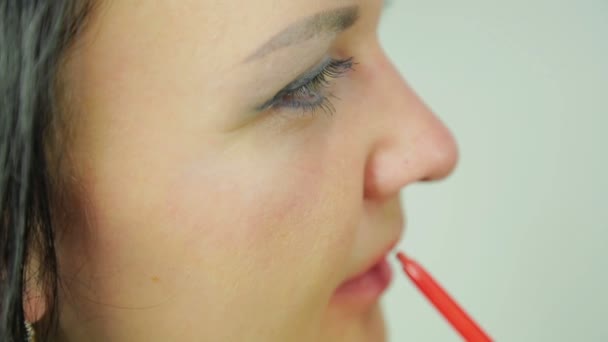 En ung kvinnlig brunett sätter en röd kontur på läpparna. Profil — Stockvideo