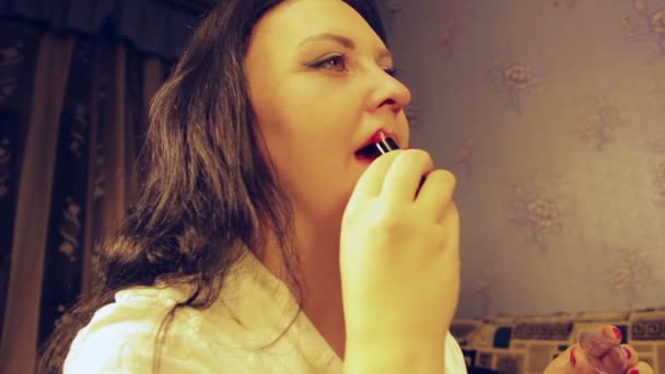 A young woman in a white robe paints her lips with bright red lipstick — Stock Video