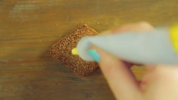 Uma mão segura um tubo de tinta de cozinha e desenha rostos engraçados nos biscoitos de chocolate com tinta amarela — Vídeo de Stock