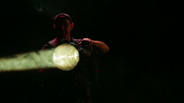 Un illuminatore maschio dirige un fascio di luce da un faretto di profilo — Video Stock