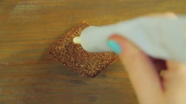 Una mano sostiene un tubo de pintura culinaria y dibuja un signo porcentual en la galleta de chocolate con pintura amarilla — Vídeos de Stock