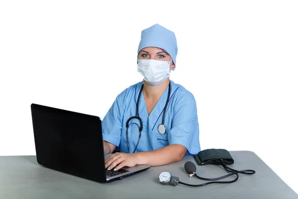 Женщина-врач со стетоскопом в медицинской маске за столом печатает на компьютере на белом фоне . — стоковое фото