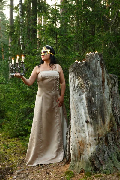 Waldfee im hellen Kleid mit Maske im Gesicht im Wald mit Kerzenständer. Gesamtplan. — Stockfoto