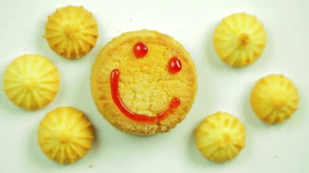 Galletas de mantequilla con pintura culinaria pintadas con un emoticono divertido y rodeadas de pequeñas galletas. Movimiento en círculo. Hecho a mano . — Vídeo de stock