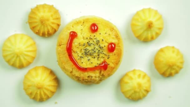 Μπισκότα βουτύρου με γαστριμαργικές μπογιά ζωγραφισμένα με μια αστεία φατσούλα και περιβάλλεται από μικρά κουλουράκια. Κίνηση σε έναν κύκλο — Αρχείο Βίντεο