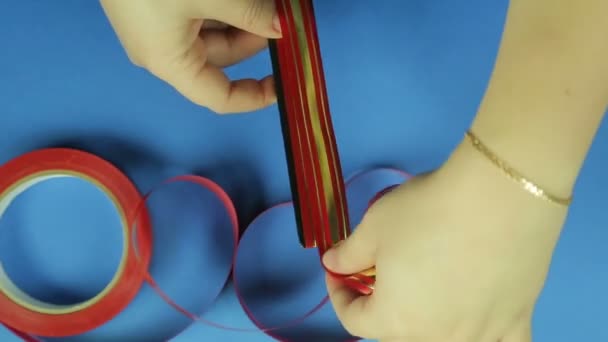 女人的手正在为一条红色丝带的弓做一个空白 蓝色背景 — 图库视频影像
