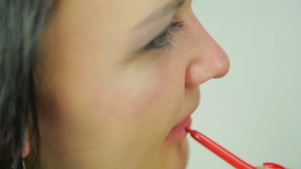 Uma jovem morena feminina coloca um contorno vermelho em seus lábios. Perfil. Close-up . — Vídeo de Stock