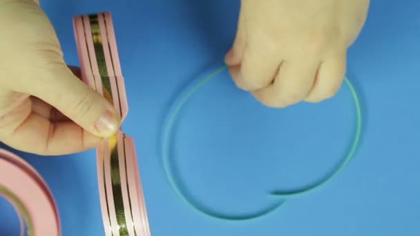 女性の手は、ギフト弓のピンクのブランクにピンクの三つ編みと関連付けられています。青色の背景 — ストック動画