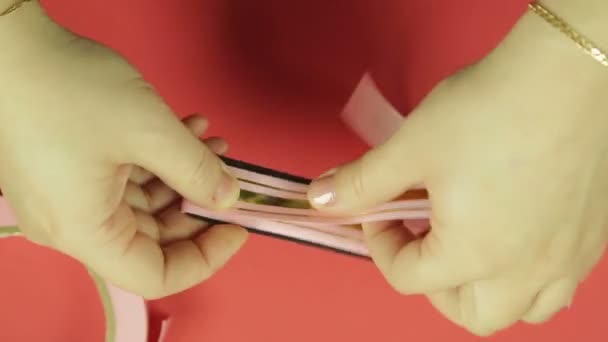Γυναικεία χέρια το τύλιγμα ένα ροζ κορδέλα στο πρότυπο για την κατασκευή ένα τόξο δώρο. Κόκκινο φόντο — Αρχείο Βίντεο