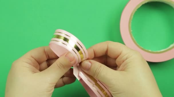 Жіночі руки утворюють заготовку рожевої стрічки для подарункового лука на зеленому тлі — стокове відео