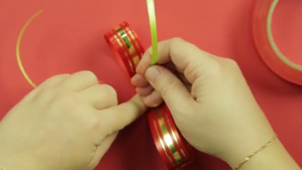 Las manos de las mujeres están atadas con una trenza rosa con un blanco rosado para un lazo de regalo. Fondo rojo — Vídeos de Stock