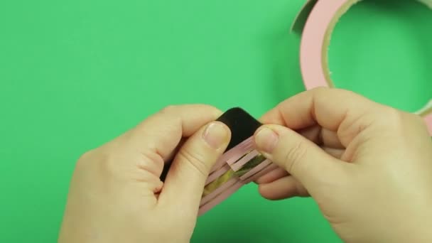 Female hands wrapping a pink ribbon pattern on a green background — Stock Video