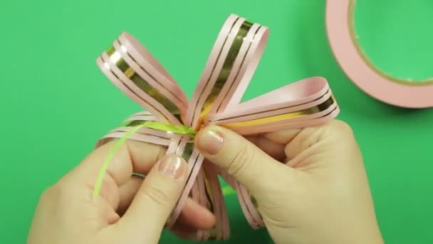 Γυναικεία χέρια δίνουν σχήμα σε ένα ροζ κορδέλα τόξο σε πράσινο φόντο — Αρχείο Βίντεο