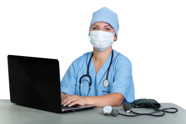 Женщина-врач со стетоскопом в медицинской маске за столом за компьютером на белом фоне . — стоковое фото