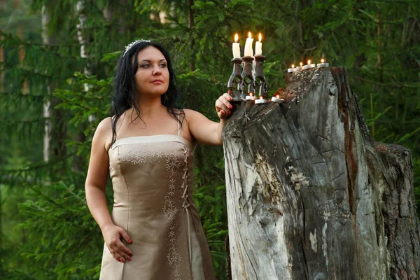 Waldfee im hellen Kleid an einem großen Baumstumpf mit Kerzenständer. — Stockfoto