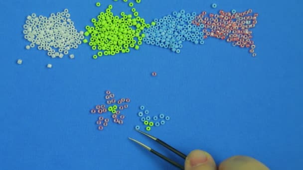 Female hand on a blue background pokes out flowers from multi-colored beads. Close-up. — Stock Video