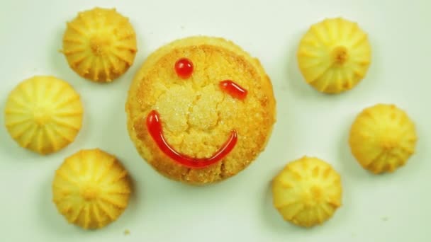 Biscoitos de manteiga com tinta culinária pintados com um emoticon engraçado e cercados por pequenos biscoitos. Movimento em círculo . — Vídeo de Stock