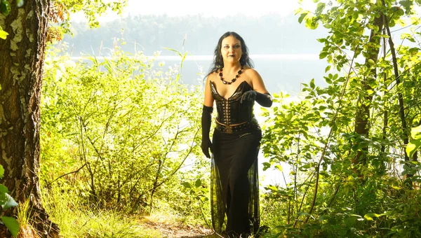 A young woman is a sorceress in black by the lake. Halloween. — Stock Photo, Image