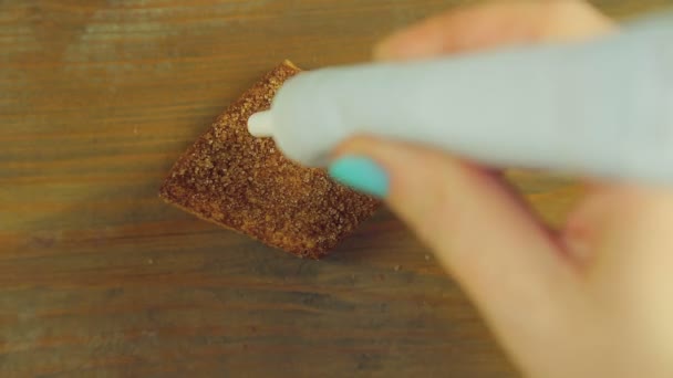Une main tient un tube de peinture de cuisson et dessine des émoticônes drôles avec de la peinture jaune sur un cookie aux pépites de chocolat — Video