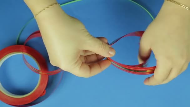 As mãos femininas cortam os cantos com uma tesoura para um laço de presente de fita vermelha. Fundo azul — Vídeo de Stock