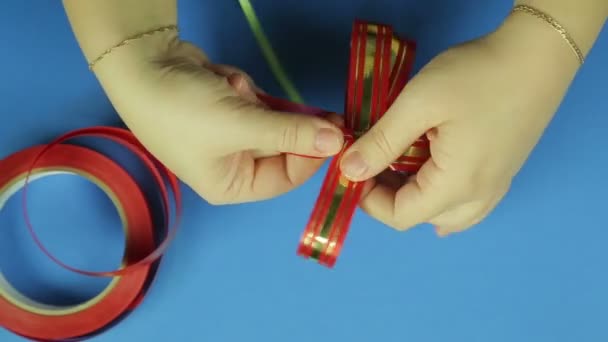 女性の手は、赤いリボンの弓に形を与えます。青色の背景 — ストック動画