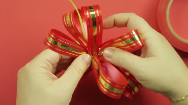 Las manos de mujer enderezan los pétalos de un lazo de regalo de cinta rosa y le dan la forma de un lazo. Fondo rojo — Vídeos de Stock