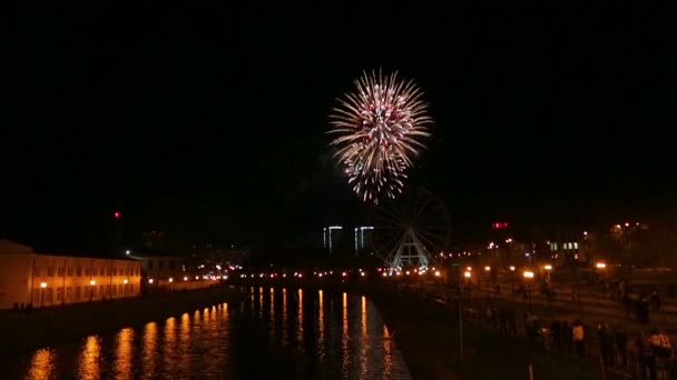 Brillantes fuegos artificiales hermosos en la ciudad en el terraplén en el cielo nocturno se refleja en el río — Vídeo de stock