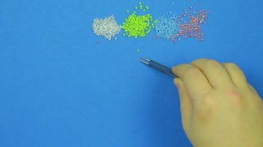 Mavi bir arka plan üzerinde el boncuk cımbızla bırakır. Yakın çekim. El yapımı