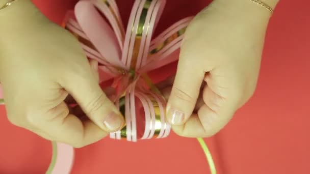 女性の手はまっすぐにピンクリボン ギフト弓の花びらとの弓の形を与えます 赤の背景 — ストック動画