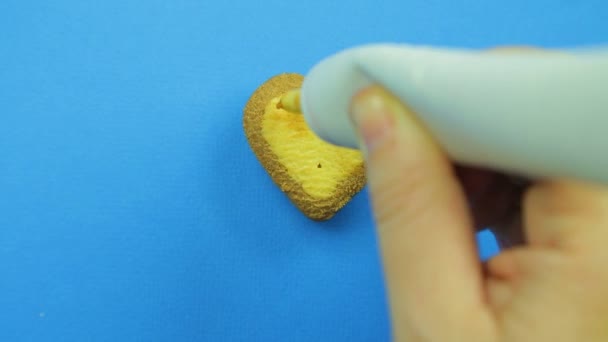 Female hand paints heart-shaped cookies on a blue background with a brown tube icing funny faces. Handmade. — Stock Video