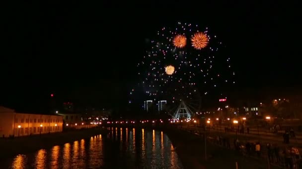 Brillantes fuegos artificiales en la ciudad en el terraplén en el cielo nocturno contra el telón de fondo de la rueda de la fortuna — Vídeo de stock