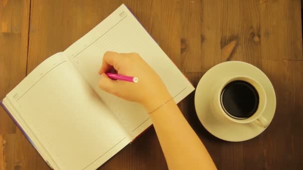 Het meisje schrijft in het dagboek het woord liefde met een roze vilt-tip pen en drinken koffie. Tijd ronden — Stockvideo