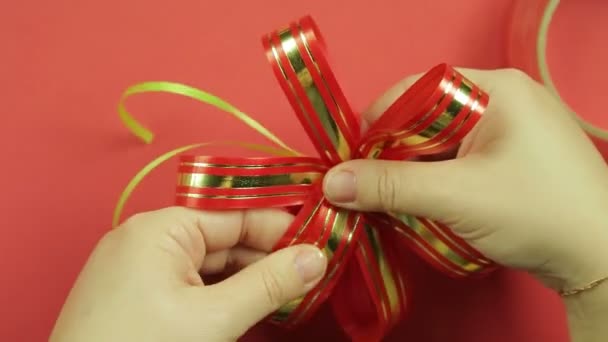 Womens handen de bloemblaadjes van een roze lint cadeau boog rechtzetten en de vorm van een boog te geven. Rode achtergrond. — Stockvideo