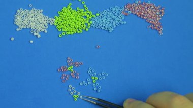 Mavi bir arka plan üzerinde el çok renkli boncuk çiçek dışarı cımbızla pokes. Yakın çekim.