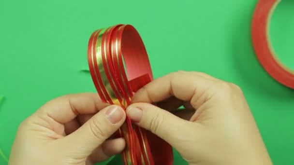 Жіночі руки формують порожню червону стрічку для виготовлення подарункового лука. Зелений фон — стокове відео