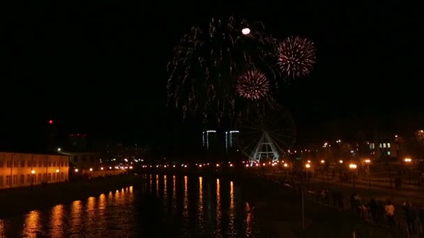 Heldere vuurwerk in de stad in de nachtelijke hemel over de rivier aan de kade. — Stockvideo