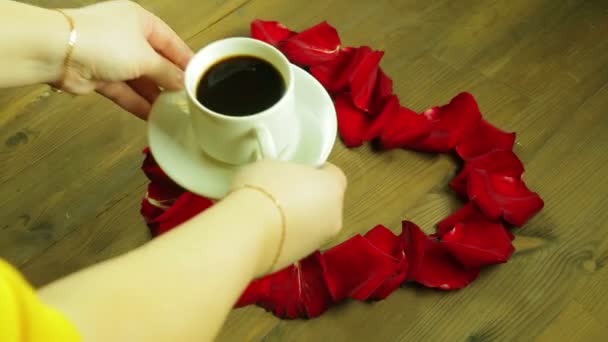 Flickan sätter mitt i hjärtat av rosenblad med en kopp kaffe. — Stockvideo